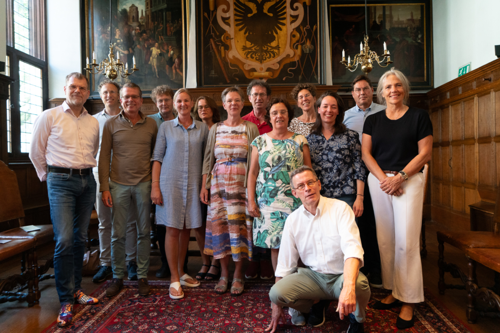 Een groepsportret van de directeuren die aan OPEN verbonden zijn, en de gastvoorzitter van OPEN. Ze staan in twee rijen naast elkaar in de oude trouwzaal in het Stadshuis in Naarden.